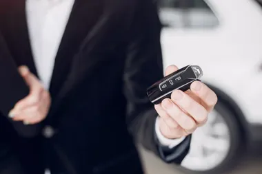 Dłoń w garniturze trzyma pilot-kluczyk do samochodu (przyciski zamka i bagażnika)